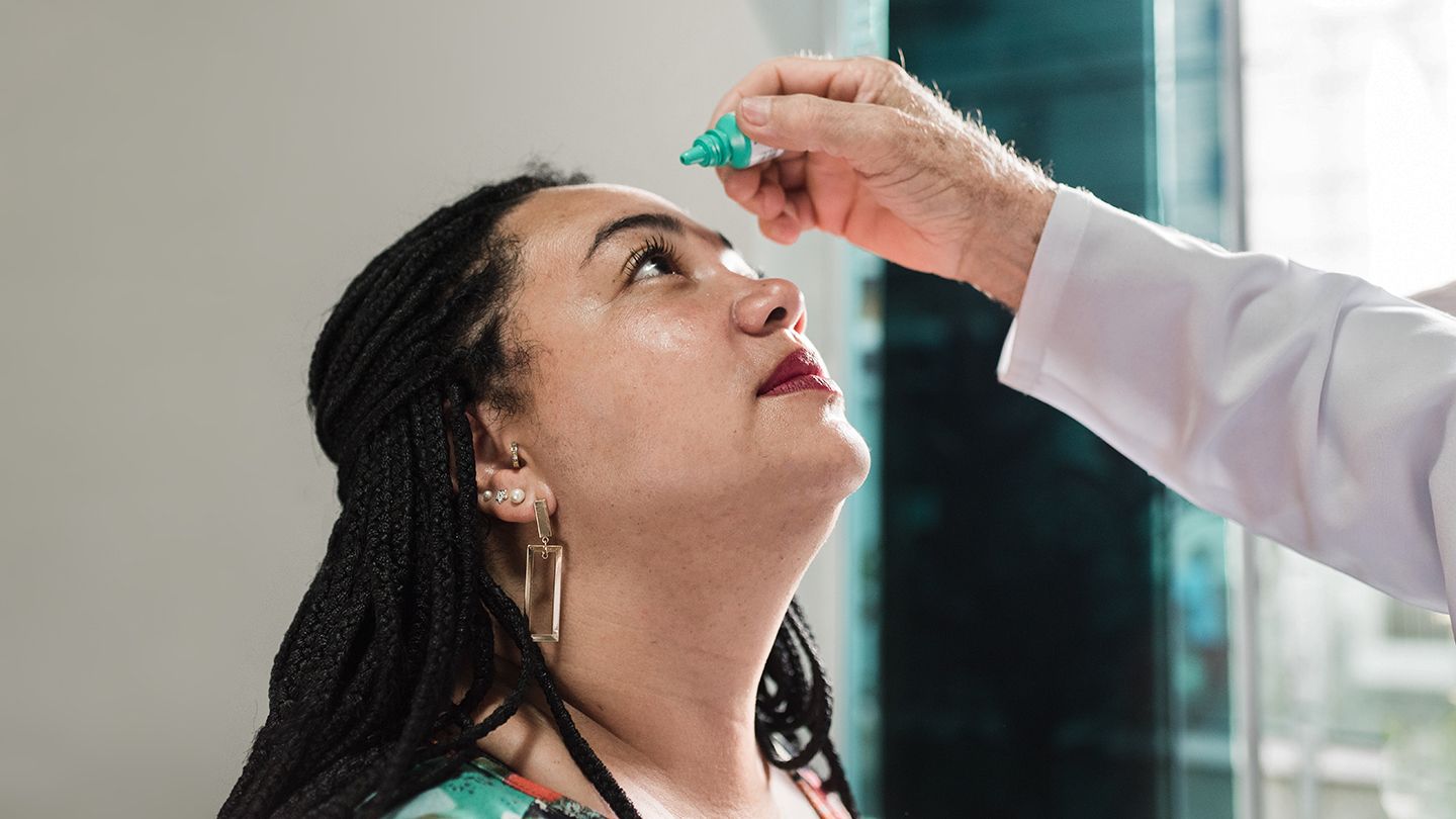 ophthalmologist dripping eye drops into woman patient eye during consultation